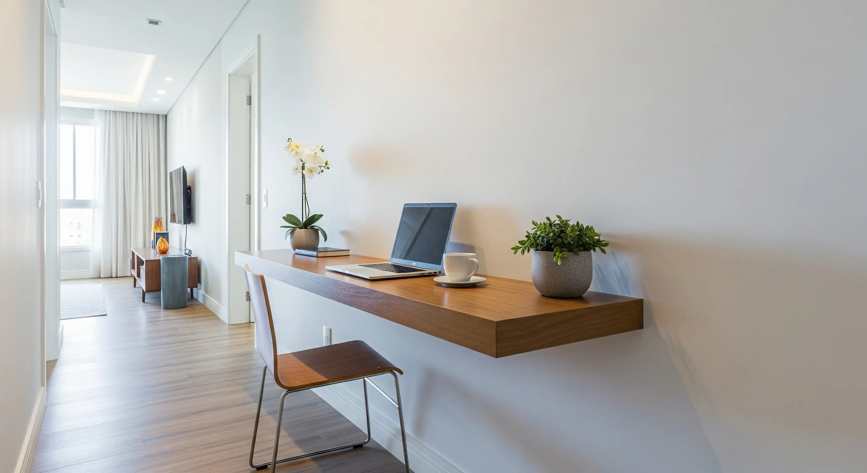 Um corredor bem iluminado com uma prateleira suspensa de madeira servindo como uma mesa de trabalho minimalista, com um notebook e uma cadeira fina.